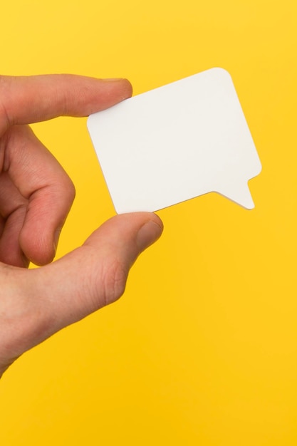 Bolha de fala branca em branco realizada em uma mão em um fundo amarelo brilhante