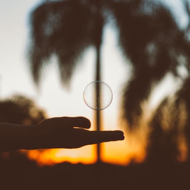 Foto bolha de sabão sobre a mão cortada de uma pessoa na praia durante o pôr do sol