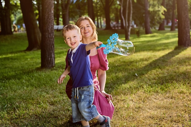 Bolhas como jogo para mãe e filho sorridentes no parque público.