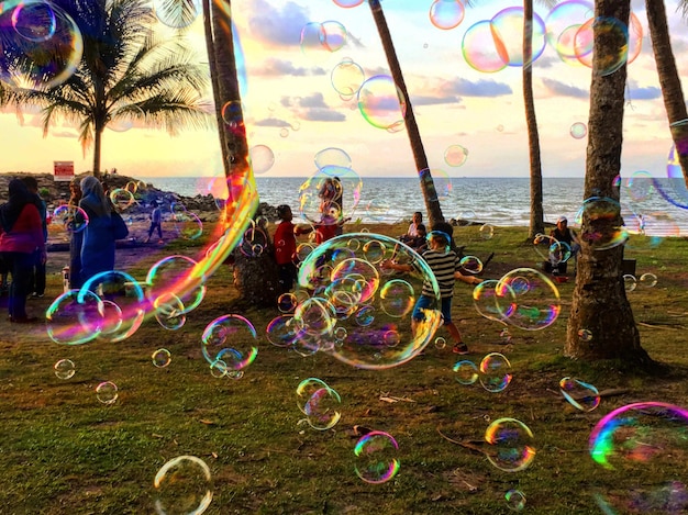 Foto bolhas no ar com pessoas na praia durante o pôr-do-sol