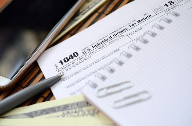 El bolígrafo, el cuaderno, el teléfono inteligente y los billetes en dólares se encuentran en el formulario de impuestos 1040 EE. UU.