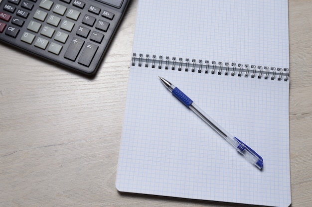 Un bolígrafo y una microcalculadora se encuentran en un cuaderno cuadrado. de cerca.