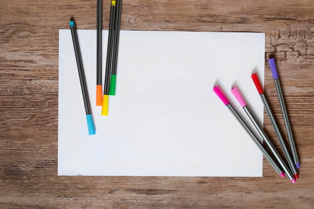 Bolígrafos de colores y hoja de papel en blanco sobre fondo de madera