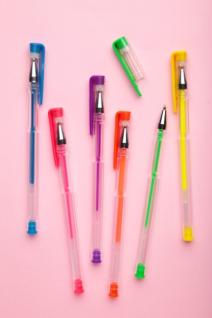 Bolígrafos de diferentes colores sobre superficie rosa con espacio de copia