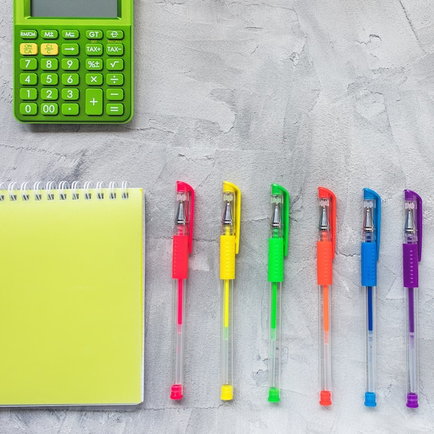 Bolígrafos de gel multicolores, cuaderno y calculadora.