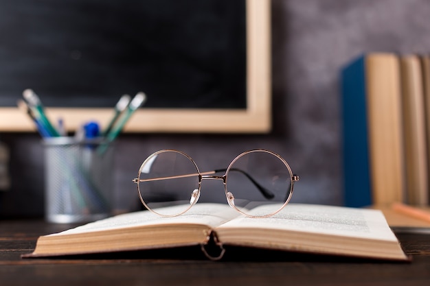 Bolígrafos, lápices, libros y vasos sobre la mesa, con el telón de fondo de la pizarra