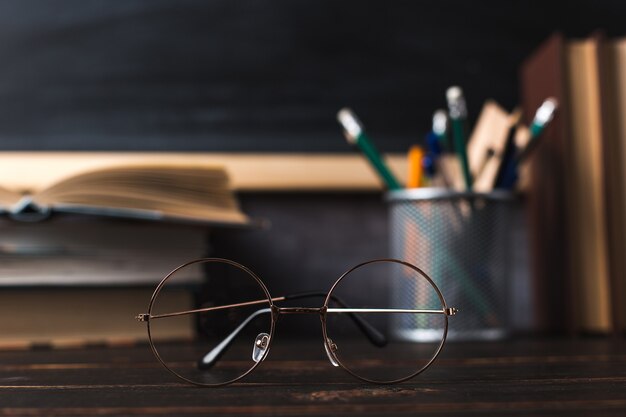 Bolígrafos, lápices, libros y vasos sobre la mesa, con el telón de fondo de la pizarra