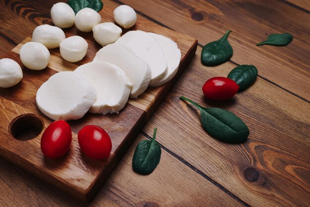 Bolinhas de queijo mozzarella brancas, folhas de espinafre e tomates em uma placa de madeira