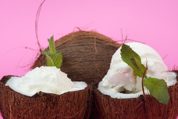 Bolinhas de sorvete de baunilha em metades de coco fresco, decoradas com folhas de hortelã em um fundo rosa.