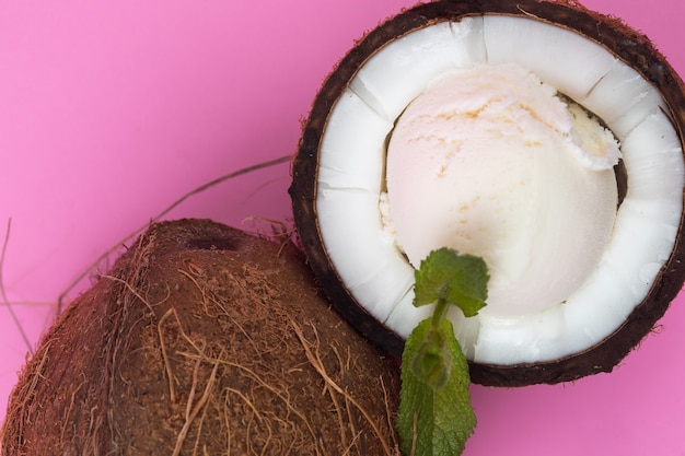 Bolinhas de sorvete de baunilha em metades de coco fresco, decoradas com folhas de hortelã em um fundo rosa.