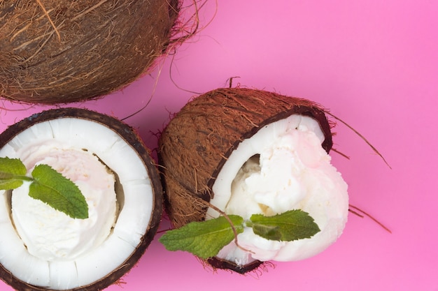 Bolinhas de sorvete de baunilha em metades de coco fresco, decoradas com folhas de hortelã em um fundo rosa.