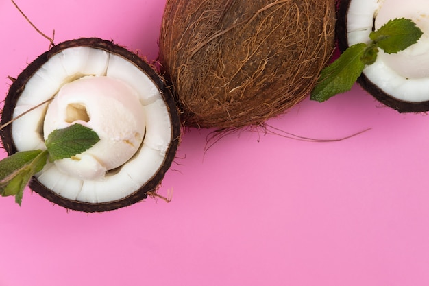 Bolinhas de sorvete de baunilha em metades de coco fresco, decoradas com folhas de hortelã em um fundo rosa.