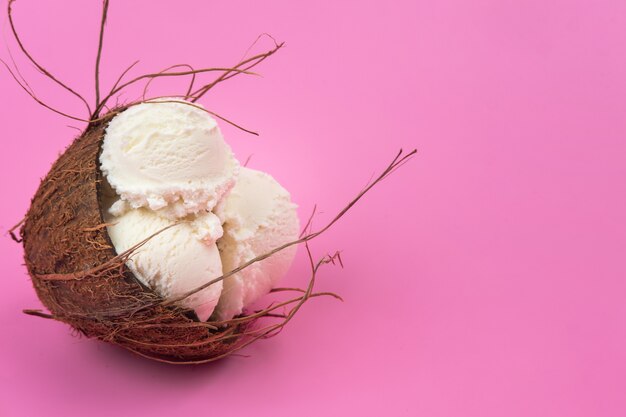 Bolinhas de sorvete de baunilha em um coco vazio decorado com folhas de hortelã em um fundo rosa