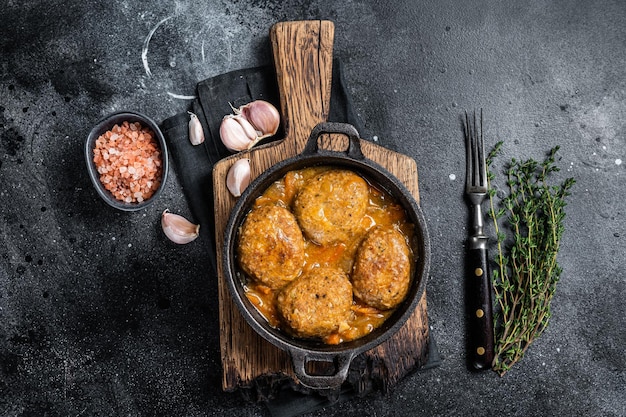 Bolinho de peixe com atum em molho de tomate em uma panela. Fundo preto. Vista do topo.