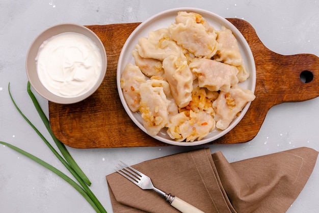 Bolinhos caseiros vareniki varenyky pyrohy com repolho guisado frito com cebola na chapaPrato nacional popular ucraniano tradicionalcozinha servida com creme de leite na placa de madeira backgound cinza