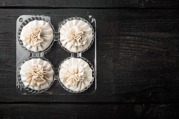 Bolinhos chineses Baozi crus. Conjunto de bolinhos azianos, em bandeja de plástico, sobre mesa de madeira preta