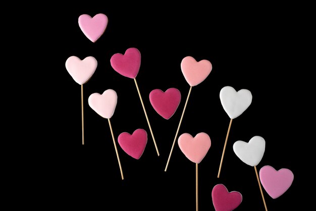 Bolinhos cor-de-rosa e brancos em uma vara na forma dos corações em um preto isolado. dia dos namorados.