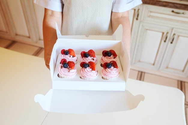 Bolinhos cremosos apetitosos com frutas frescas na caixa nas mãos da mulher, conceito de entrega de sobremesas.