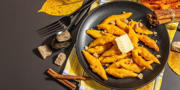 Bolinhos de abóbora preguiçosos, nhoque com manteiga e açúcar mascavo. Prato quente de outono, comida doce e saudável. Fundo de concreto de pedra preta, luz forte moderna, sombra escura, formato de banner