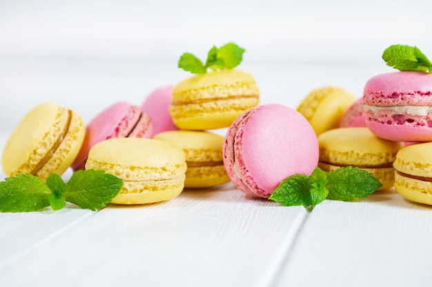 Bolinhos de amêndoa e folhas de hortelã coloridos na tabela de madeira branca.