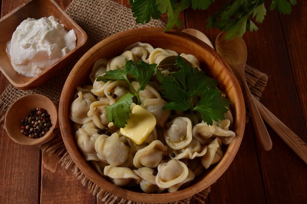 Bolinhos de carne caseiros servidos com creme de leite e salsa fresca no prato. Comida tradicional russa - pelmeni