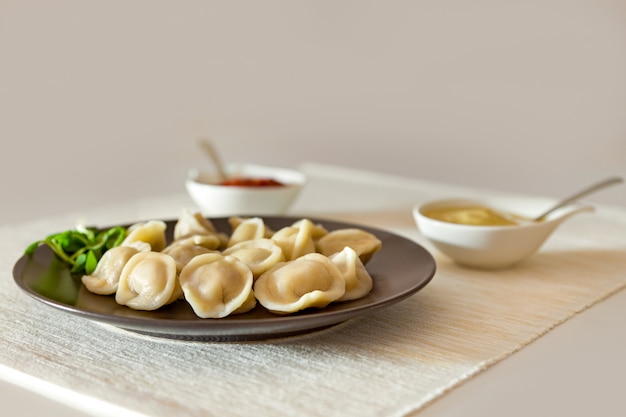 Bolinhos de carne pelmeni comida russa com mostarda e molho de tomate em um prato marrom.