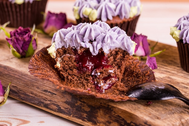 Bolinhos de chocolate em uma mesa de madeira com flores de cremama, com geléia de frutas dentro.