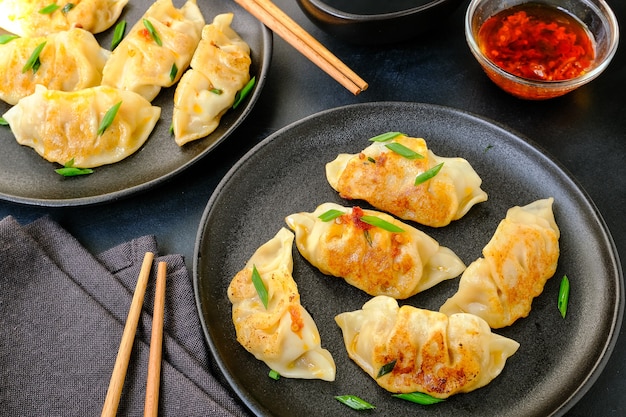 Foto bolinhos de jiaozi gyoza cozidos em pratos pretos com molho de soja e óleo de pimenta