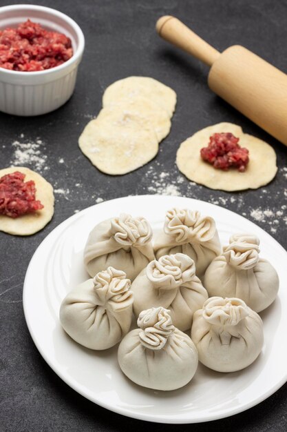 Bolinhos de khinkali crus na chapa branca Carne picada na tigela Pedaços de massa e carne na massa Vista superior Fundo preto