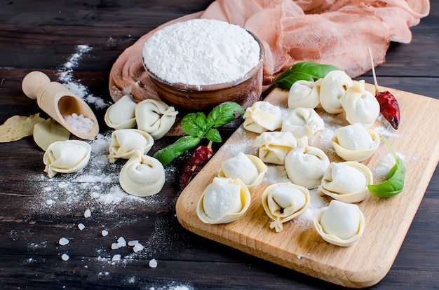 Bolinhos de massa crus com carne com farinha em fundo escuro