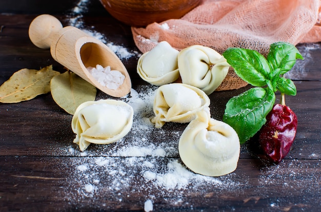 Bolinhos de massa crus com carne com farinha no fundo escuro