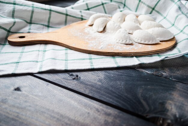 Bolinhos de massa crus polvilhados com farinha sobre uma tábua de cozinha e uma toalha listrada