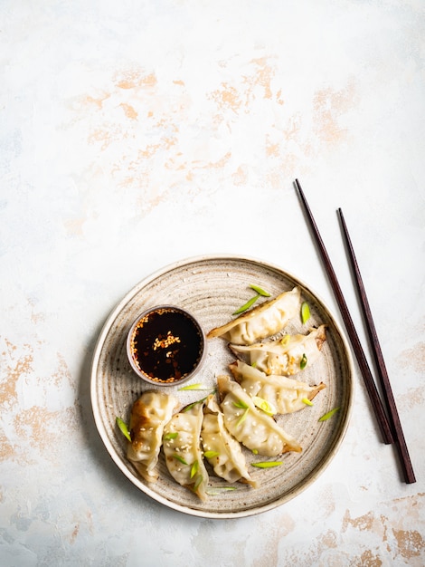 Bolinhos de massa tradicionais chineses - gyoza com carne de porco e legumes em um prato redondo com molho de soja em uma tigela.