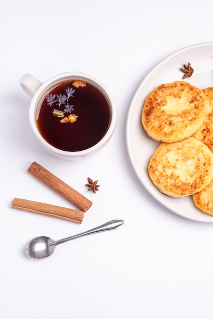 Bolinhos de queijo cottage com chá preto quente aromático, clima de café da manhã de natal com anis e canela em fundo branco, vista de cima