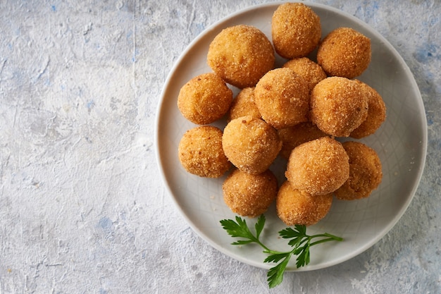 Bolinhos de queijo frito, aperitivo com ervas e molhos em um prato sobre uma mesa cinza