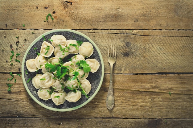 Bolinhos de ravióli de pelmeni russo tradicional com carne na mesa de madeira com farinha salsa ovos de codorna pimenta alecrim folha de louro e especiarias Vista superior Efeito tonificado Copyspace