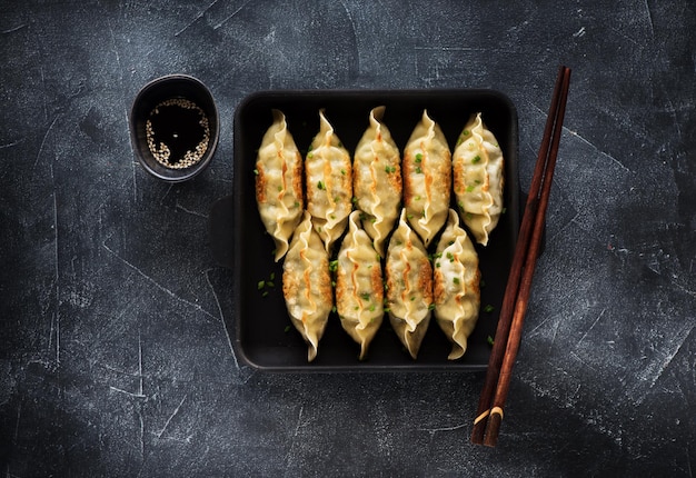 Bolinhos fritos Gyoza na panela, molho de soja, pauzinhos em fundo escuro de pedra, vista superior