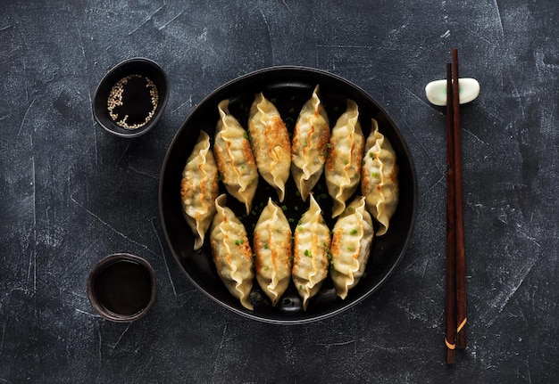 Bolinhos fritos Gyoza na panela, molho de soja, pauzinhos em fundo escuro de pedra, vista superior