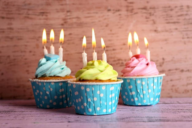 Bolinhos saborosos com velas na mesa violeta contra fundo de madeira