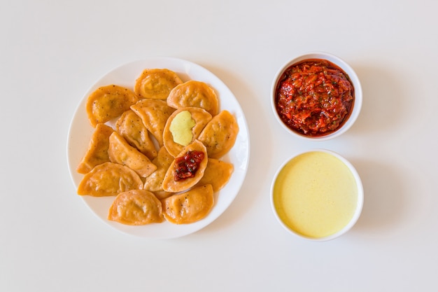 Bolinhos tradicionais de vareniki de comida russa e ucraniana com mostarda e molho de tomate em um prato branco.