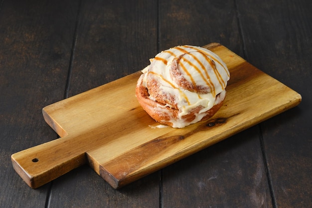 Bollo de canela con caramelo y glaseado sobre tabla de servir de madera