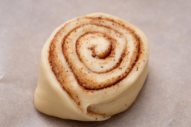 Bollo de canela cruda sobre papel de horno. Cocinar en casa sabrosos bollos con canela en polvo