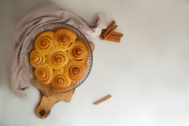 bollo de canela con glaseado y palitos de canela con un vaso de leche sobre un fondo gris clarovista superior