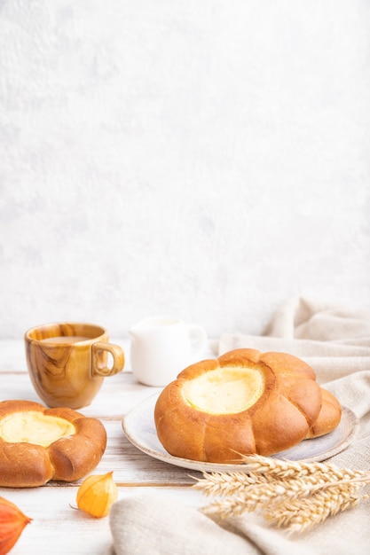 Bollo de crema agria con taza de café sobre un fondo blanco de madera y hormigón y textil de lino. Vista lateral, primer plano, enfoque selectivo, espacio de copia.