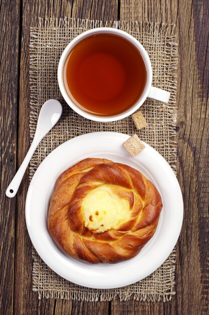 Bollo dulce con crema y té en la mesa de madera