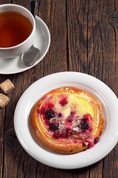 Bollo con mermelada y natillas y taza de té en la mesa de madera oscura