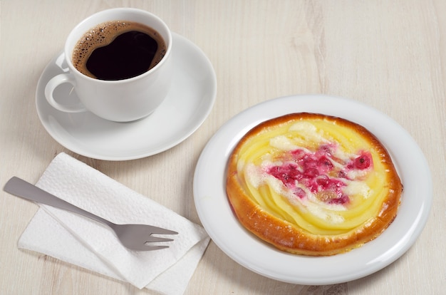 Foto bollo con natillas y bayas en plato y taza de café en la mesa de madera clara