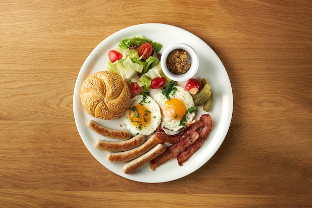 Bollo de salchichas de huevo y ensalada en un gran plato blanco sobre una mesa de madera desayuno