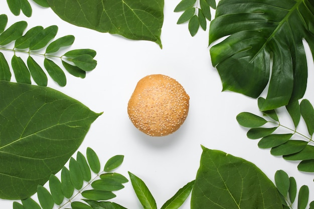 Foto bollo con semillas de sésamo sobre un fondo blanco con hojas verdes tropicales