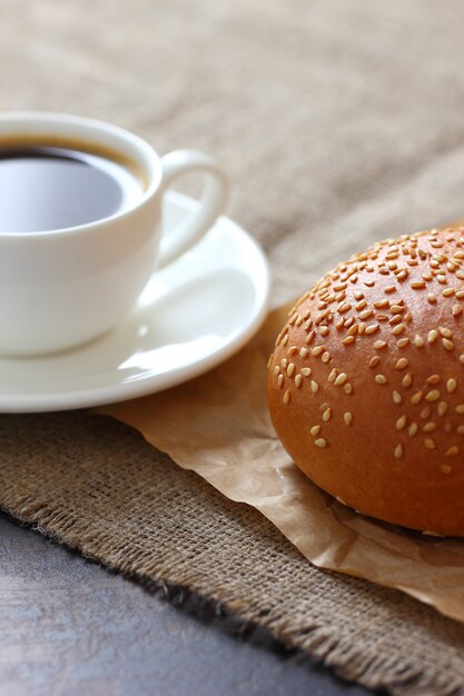 Un bollo de sésamo y una taza de café sobre papel kraft y mantel de arpillera.